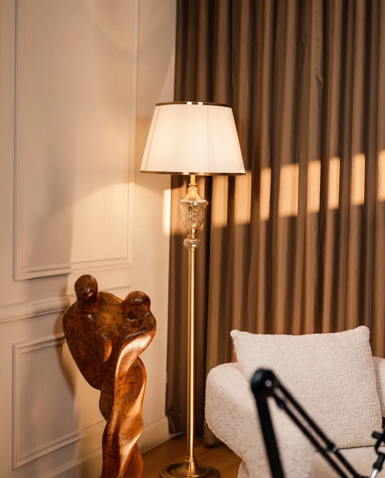 Brass floor lamp and carved wood sculpture beside a bouclé armchair — Podflix Studio, Business Bay Dubai